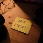 Um postit amarelo escrito "uma ideia?", em cima de uma mesa de madeira.