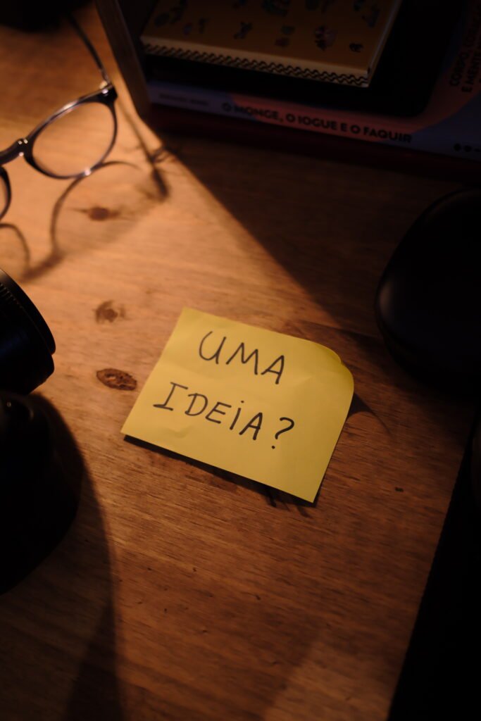 Um postit amarelo escrito "uma ideia?", em cima de uma mesa de madeira.